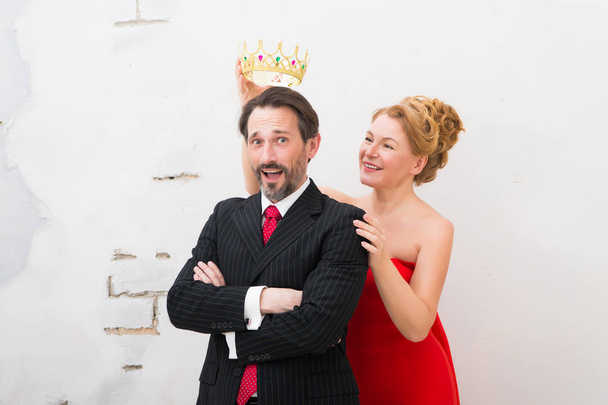 Try it on. Cheerful businessman in formal suit standing with crossed arms and being surprised while his delighted wife keeping golden crown above his head - Фото, зображення