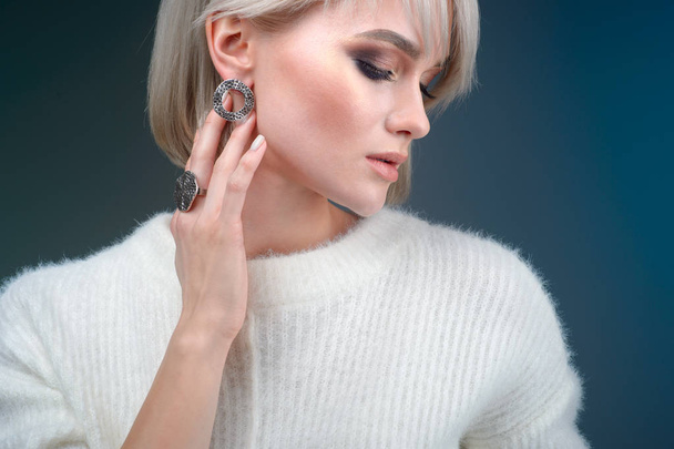 Portrait of a beautiful blonde woman with a beautiful ring and earrings posing in the studio on a blue background - Фото, зображення