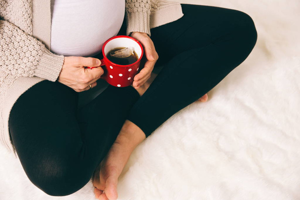 Zwangere vrouw zitten met thee in rode mok - Foto, afbeelding