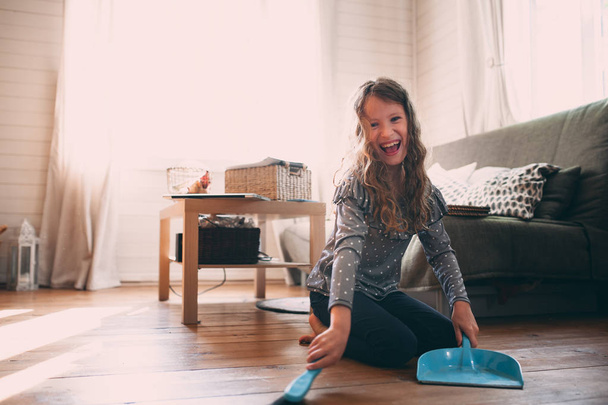 funny kid girl helping with housework and cleaning wooden floor at home - Valokuva, kuva