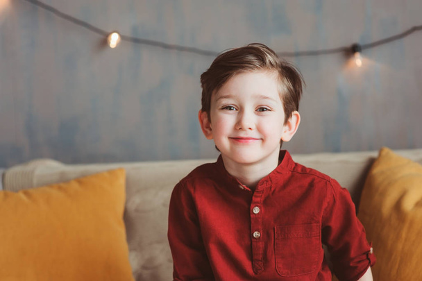 indoor portrait of happy handsome stylish child boy sitting on cozy couch in casual clothing - Foto, afbeelding