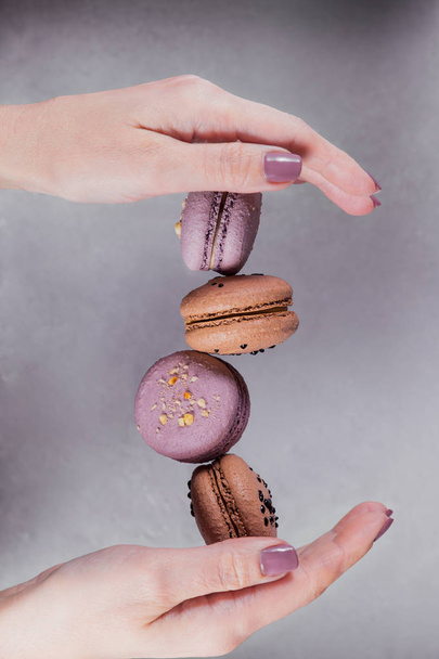Sweet french macarons cookies stacked on woman's hands against grey background. Pastel colored flying macaroons. Food, culinary and cooking concept - 写真・画像