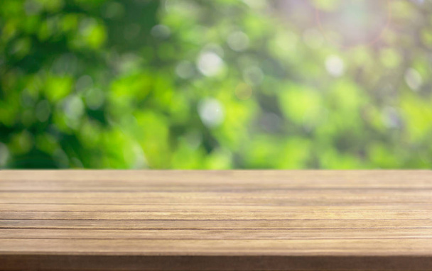 Πρότυπο φόντο για μια παρουσίαση ξύλινη επιφάνεια τραπεζιού και θαμπά φύλλα ενός δέντρου στο παρασκήνιο σε μια καλοκαιρινή ηλιόλουστη μέρα - Φωτογραφία, εικόνα