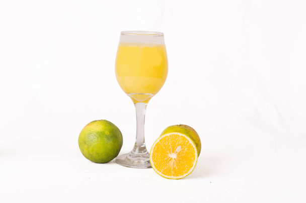 Zumo de naranja en un vaso transparente y al lado de las naranjas y una rebanada muy madura
. - Foto, imagen