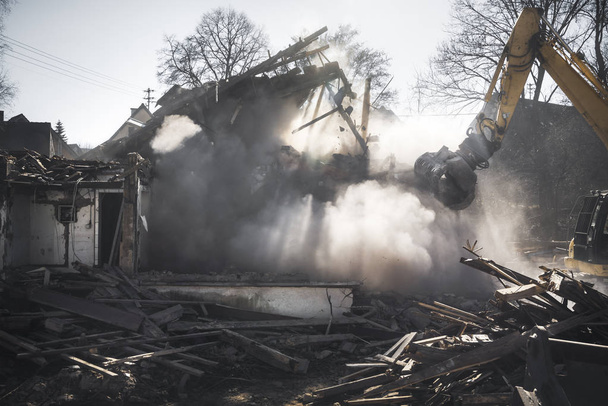 Demolizione di una vecchia casa tedesca con un escavatore. Casa che si schianta in una nube di polvere e raggi di sole. Cantiere
. - Foto, immagini
