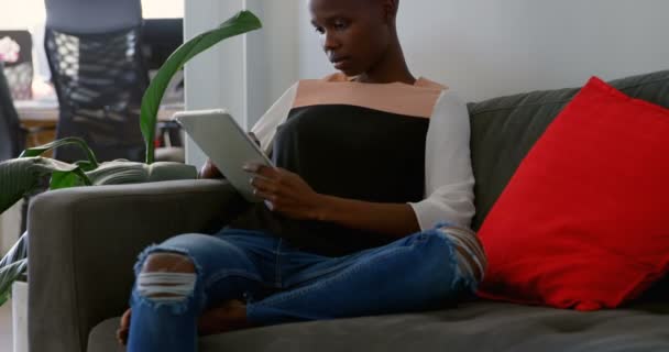 Front view of young black businesswoman working on digital tablet and sitting on couch in office. She is scrolling and checking mail 4k - Video
