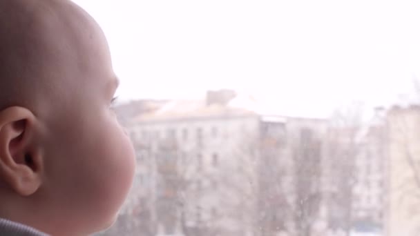 Happy baby looks out the window. The child rejoices smiling. Draws a hand on the window. Slow Motion - Materiał filmowy, wideo