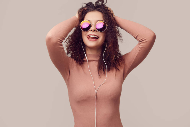 Modeporträt eines hellen wunderschönen positiven Mädchens mit lockigem Haar, das im Studio Musik über Kopfhörer hört - Foto, Bild