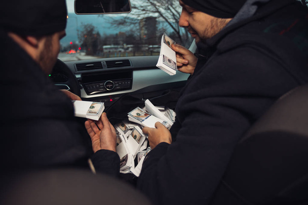 Después del robo exitoso del banco, los ladrones están sentados en el coche mostrando su dinero y celebrando la victoria sobre la ley que tenían. - Foto, Imagen