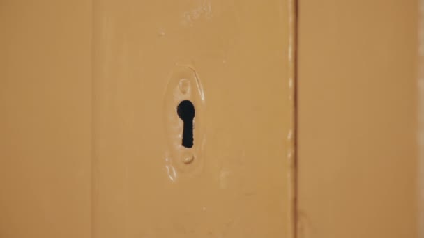 steckt die männliche Hand den Schlüssel in das Schlüsselloch, dreht den Schlüssel um und öffnet die mit beiger Ölfarbe bemalte Tür. Glühbirnen am Abend. Dunkle Tür. Primitiv einfaches Türschloss - Filmmaterial, Video