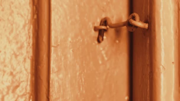 In de avond opent iemands hand een houten deur in een huis opgesloten op een haak. Gloeilampen. De houten deur is geschilderde beige. Donkere deuropening. Primitieve deurslot - Video