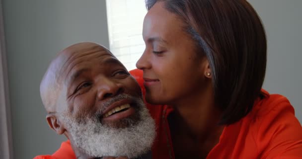Front view of mature black woman kissing on mans cheek in a comfortable home. She is embracing mature man 4k - Felvétel, videó