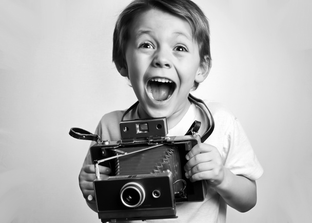 Niño pequeño sosteniendo una cámara instantánea sobre un fondo blanco
 - Foto, Imagen