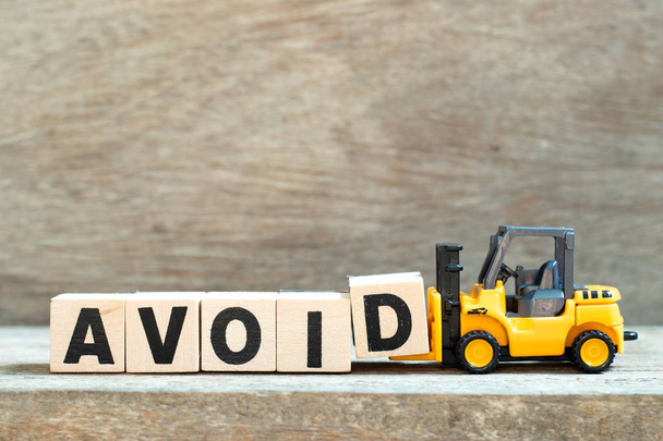 Empilhadeira de brinquedo segurar letra bloco d para completar a palavra evitar no fundo de madeira
 - Foto, Imagem