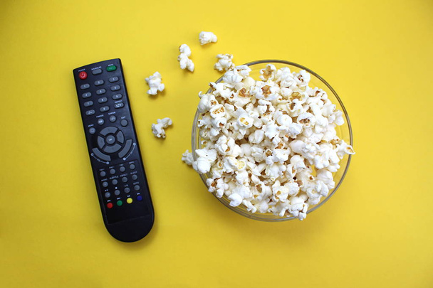On a glass plate lies salty crunchy popcorn and next to it is a TV remote - Foto, afbeelding