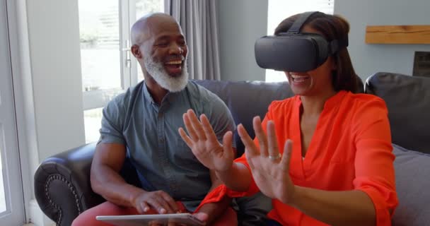 Front view of mature black woman gesturing and using virtual reality headset in comfortable home. Happy mature man using digital tablet and looking at her 4k - Materiał filmowy, wideo
