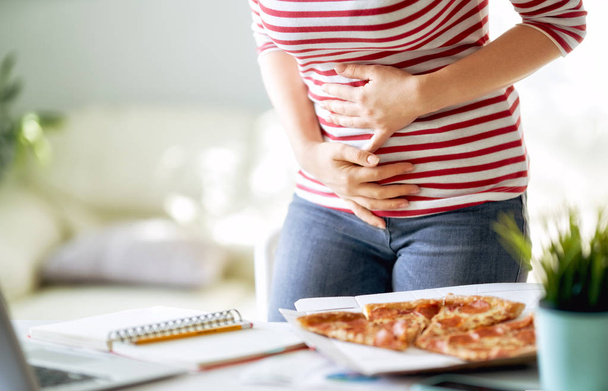 Woman eating pizza on the desk at work and having stomach problems. - Foto, Imagen