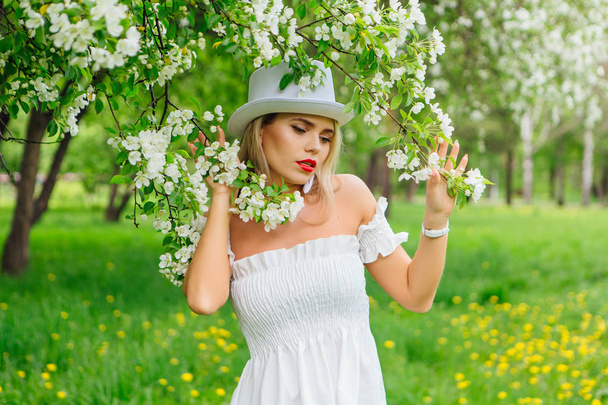 Sexy modern bride in white cylinder hat enjoing bloomin apple tree flowers - Photo, image