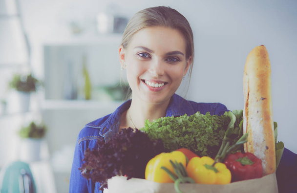 Young woman holding grocery shopping bag with vegetables .Standing in the kitchen - Foto, Imagen