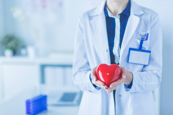 Een arts met stethoscoop onderzoek rode hart, geïsoleerd op witte achtergrond - Foto, afbeelding