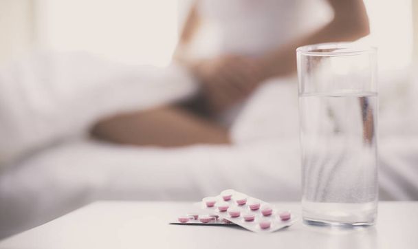 Young beautiful woman with pills lying on bed in bedroom - Photo, image