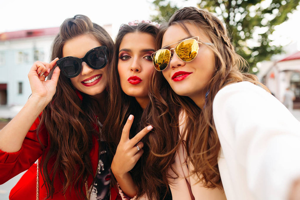 Kauniita tyttöystäviä aurinkolaseissa, jotka näyttävät rauhan merkkejä kamerassa hymyillen
. - Valokuva, kuva