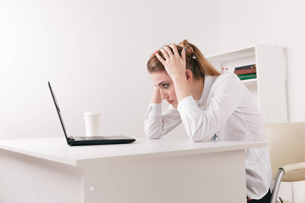 Молодая привлекательная женщина за современным рабочим столом, работает на ноутбуке, массирует виски, чтобы забыть о постоянных головных болях, шумно громкий офис давая мигрень, снимая стресс, хроническая боль, помочь успокоить
 - Фото, изображение