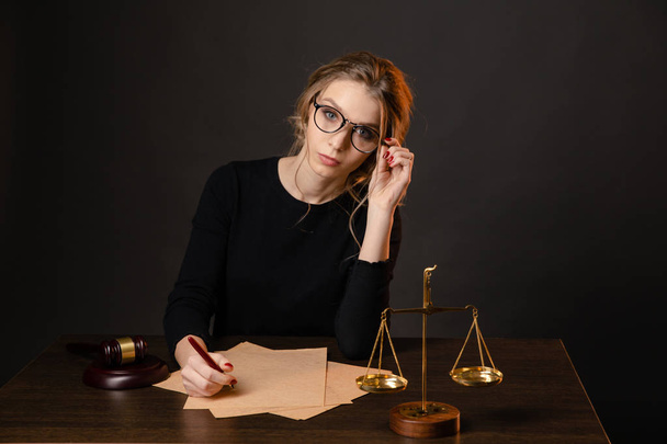 Pretty young woman in a glasses and in a black dress sitting and wrighting importaint document - Фото, изображение