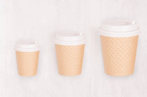 Set of three different sizes ribbed coffee kraft paper cups with cap on light wood board, top view. Mockup for branding identity, advertising and design concept. - Fotoğraf, Görsel