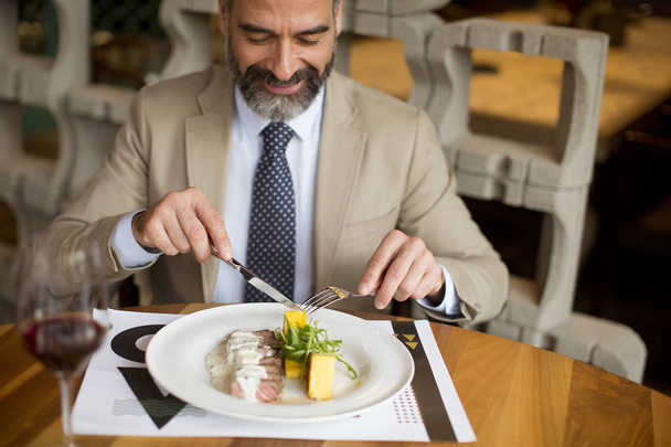 Handsome middle aged businessman having lunch and drinking red wine in restaurant - Photo, Image