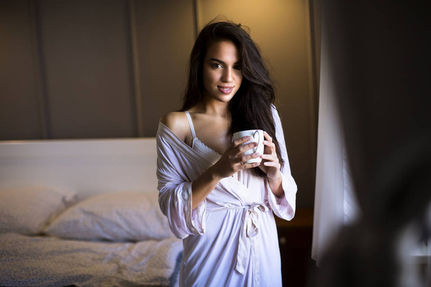 Portrait of attractive young woman with mug by the window in bedroom - Foto, Bild