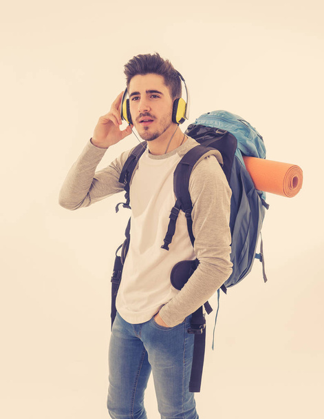 Portrait of happy young student man with backpack listening to music in headphones singing and dancing on neutral background. In positive emotions, youth traveler and happiness concept. - 写真・画像