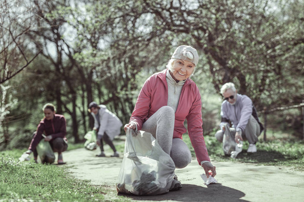 Old smiling woman in pink jacket taking disposable waste - Foto, Bild