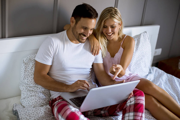 Amour jeune couple avec ordinateur portable dans le lit à la maison
 - Photo, image