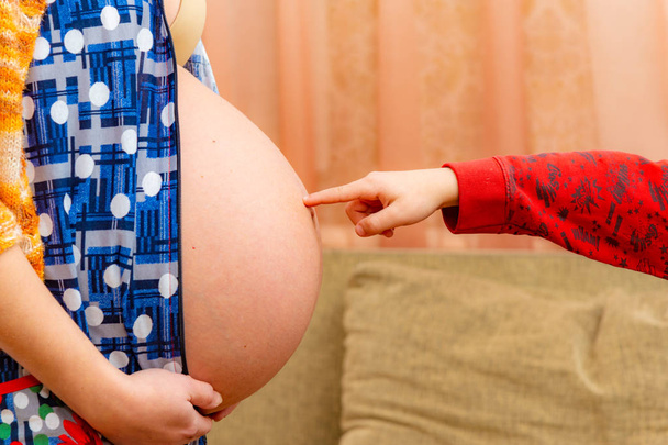 O menino coloca um dedo na barriga grande de uma mãe grávida
. - Foto, Imagem