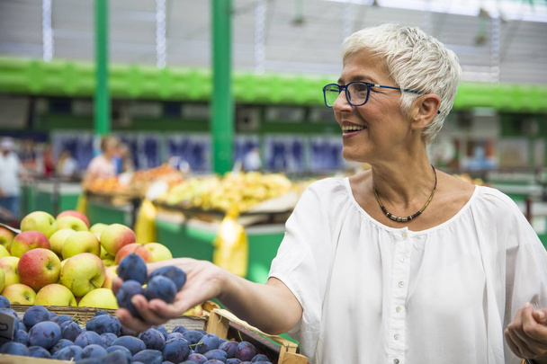 Retrato de una mujer mayor comprando fruta en el mercado
 - Foto, Imagen