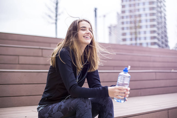 junge Frau erfrischt sich nach dem Training und trinkt Wasser im Freien - Foto, Bild
