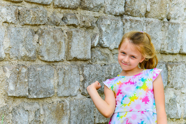 Νέα και όμορφη κοπέλα που ποζάρει σε ένα τούβλο τοίχο στο δρόμο με ένα χαμόγελο σε ένα καλοκαιρινό φόρεμα. - Φωτογραφία, εικόνα