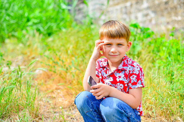 Bambino felice con uno smartphone squat e guarda la fotocamera
. - Foto, immagini
