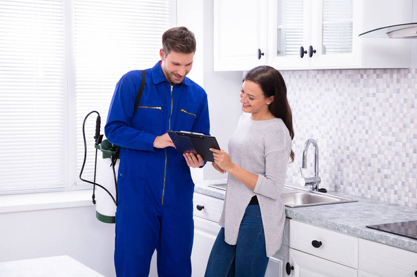 Young Male Pest Control Worker Showing Invoice To Woman In Domestic Kitchen - Foto, imagen
