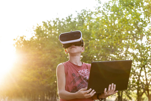 Un niño en la naturaleza en el espacio virtual, gafas VR, un bosque, un ordenador portátil
 - Foto, Imagen