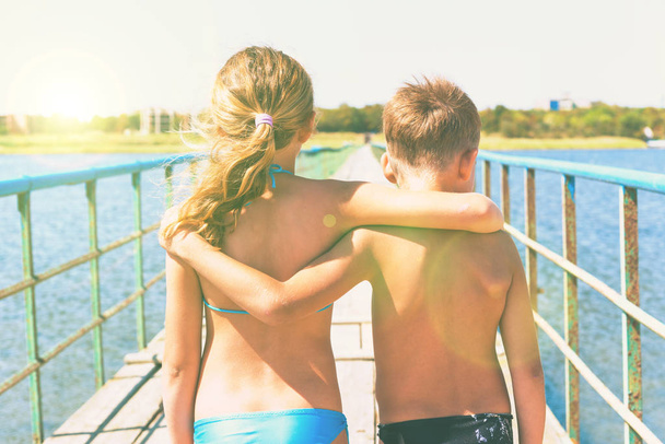 Un niño y una niña están de pie en el puente, el hermano y la hermana se abrazan en el verano en trajes de baño
. - Foto, Imagen