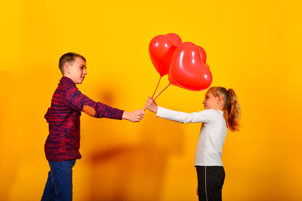 Le gars donne à la fille un tas de ballons rouges en forme de cœur, sur un fond jaune foncé pour la Saint-Valentin et le 8 Mars
. - Photo, image