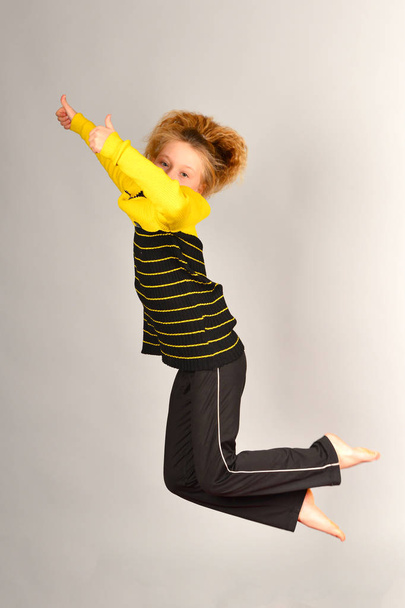 Το κορίτσι σπορ πηδάει σε διαφορετικές κατευθύνσεις σε ένα γκρίζο φόντο, μια φωτογραφία σε ένα άλμα, τα μαλλιά ανεβαίνει - Φωτογραφία, εικόνα