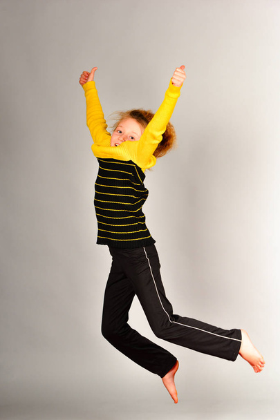 Το κορίτσι σπορ πηδάει σε διαφορετικές κατευθύνσεις σε ένα γκρίζο φόντο, μια φωτογραφία σε ένα άλμα, τα μαλλιά ανεβαίνει - Φωτογραφία, εικόνα