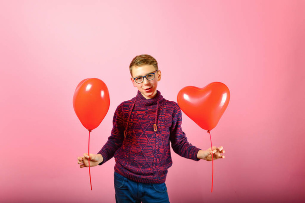 Een jongen houdt Hartvormige ballonnen op een roze achtergrond. - Foto, afbeelding