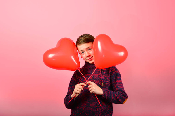 A boy holds heart-shaped balloons on a pink background. - Photo, Image