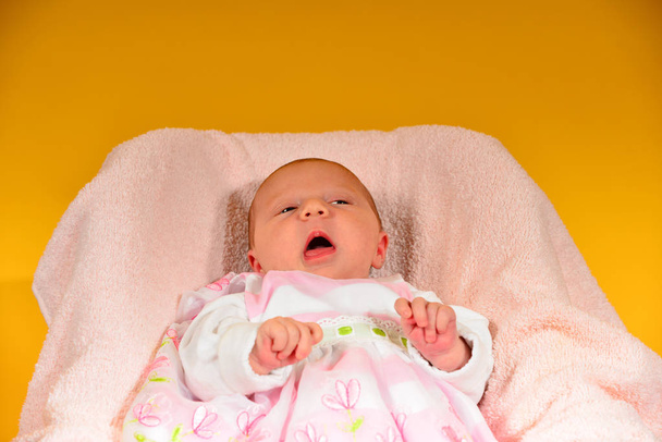 Новорожденный ребенок лежит в розовой колыбельной на желтом фоне с детскими игрушками
 - Фото, изображение