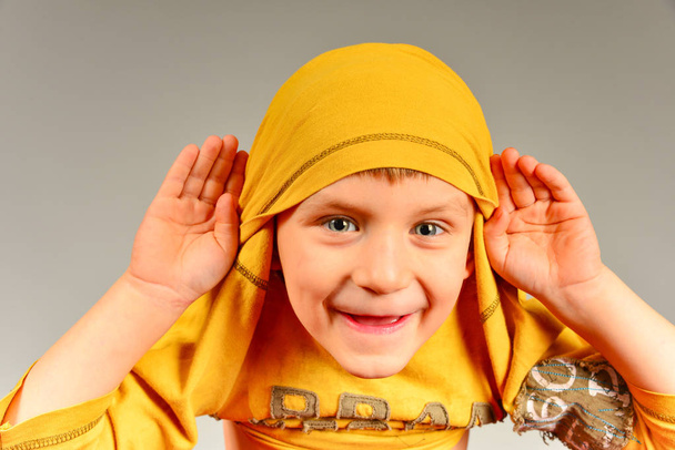 Le garçon a mis un pull jaune sur sa tête et tient ses mains près de ses oreilles, écoutant ce qu'ils lui disent
 - Photo, image