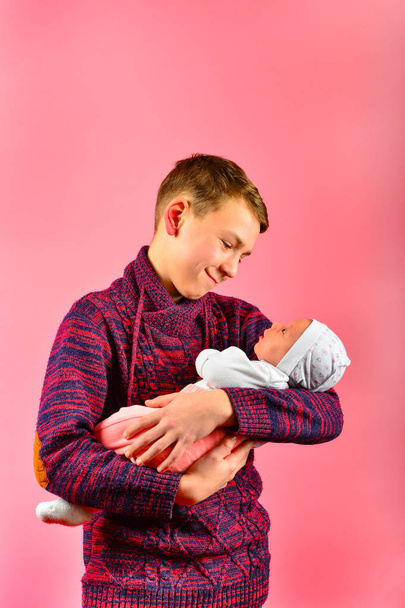 Young dad holds a newborn baby in his arms in the studio on a pink background - Fotó, kép